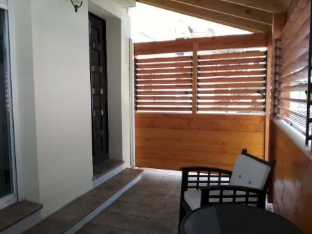 Espace extérieur avec un auvent, une porte en bois, un mur en bois et un coin détente avec une table et une chaise.