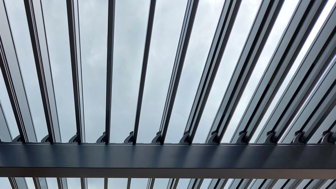 Vue en contreplongée d’une structure en métal avec des lames, laissant entrevoir un ciel nuageux.