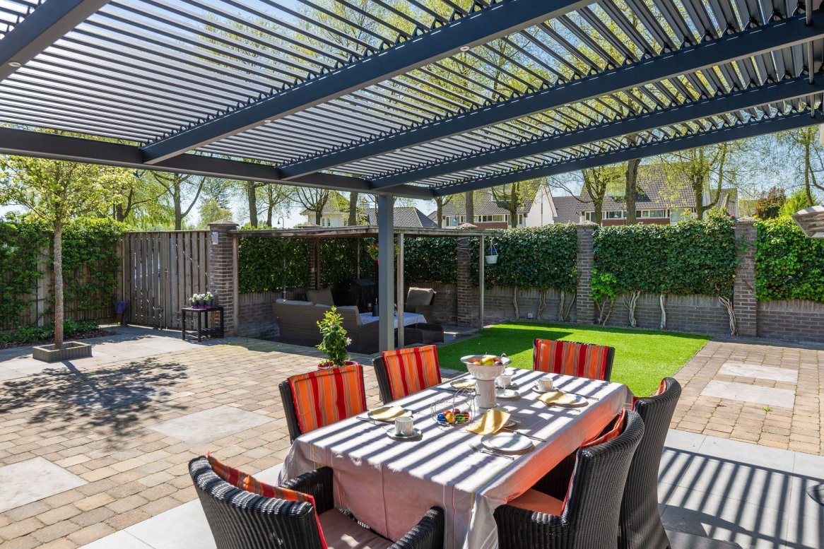 Table à manger élégante sous une pergola, entourée d’un jardin verdoyant, idéale pour les repas en plein air.