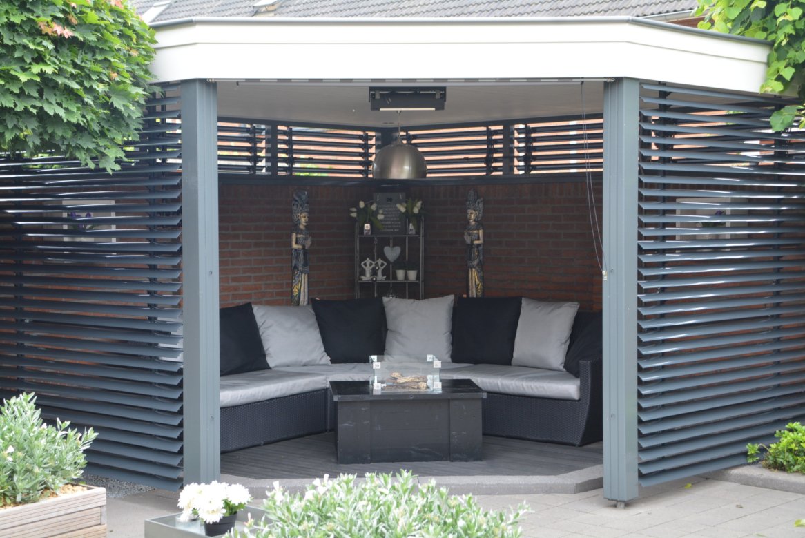 Espace lounge extérieur moderne avec canapé gris et noir, table basse, lumineux et entouré de lattes en bois.