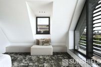 Intérieur moderne d’une chambre sous les combles, avec un grand tapis et un coin détente confortable près d’une fenêtre.