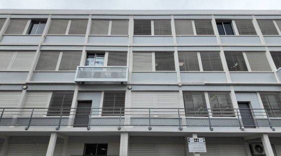 Façade d’un bâtiment moderne avec volets horizontaux, balcons et fenêtre, dans un style architectural contemporain.
