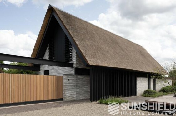 Maison moderne avec toit en chaume, façades noir et gris, intégrée dans un espace paysager minimaliste.