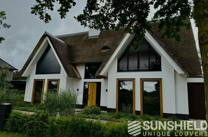 Maison moderne avec toiture en chaume, grandes fenêtres et végétation verdoyante, alliant style et design contemporain.